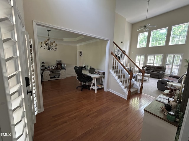 foyer entrance with dark wood-type flooring, a towering ceiling, ornamental molding, a chandelier, and stairs