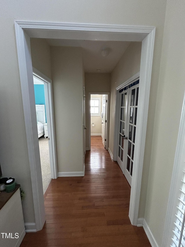 corridor with wood finished floors, baseboards, and french doors