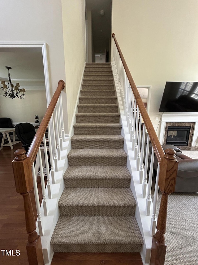 staircase with wood finished floors, a chandelier, and a high end fireplace