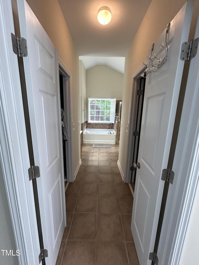hall with lofted ceiling, dark tile patterned floors, and baseboards