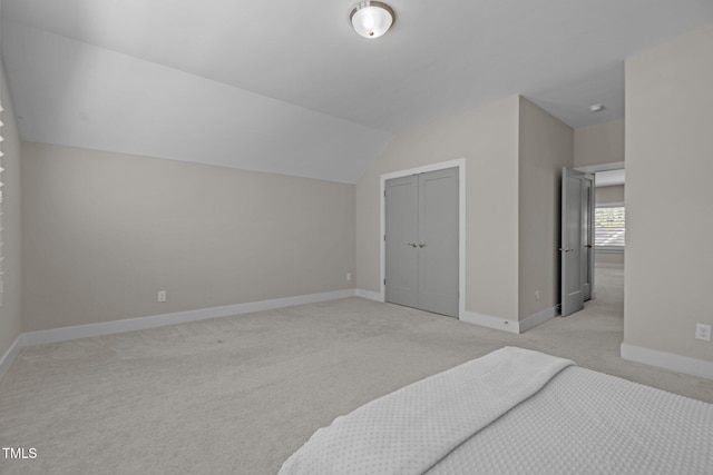 unfurnished bedroom with light colored carpet, baseboards, a closet, and vaulted ceiling