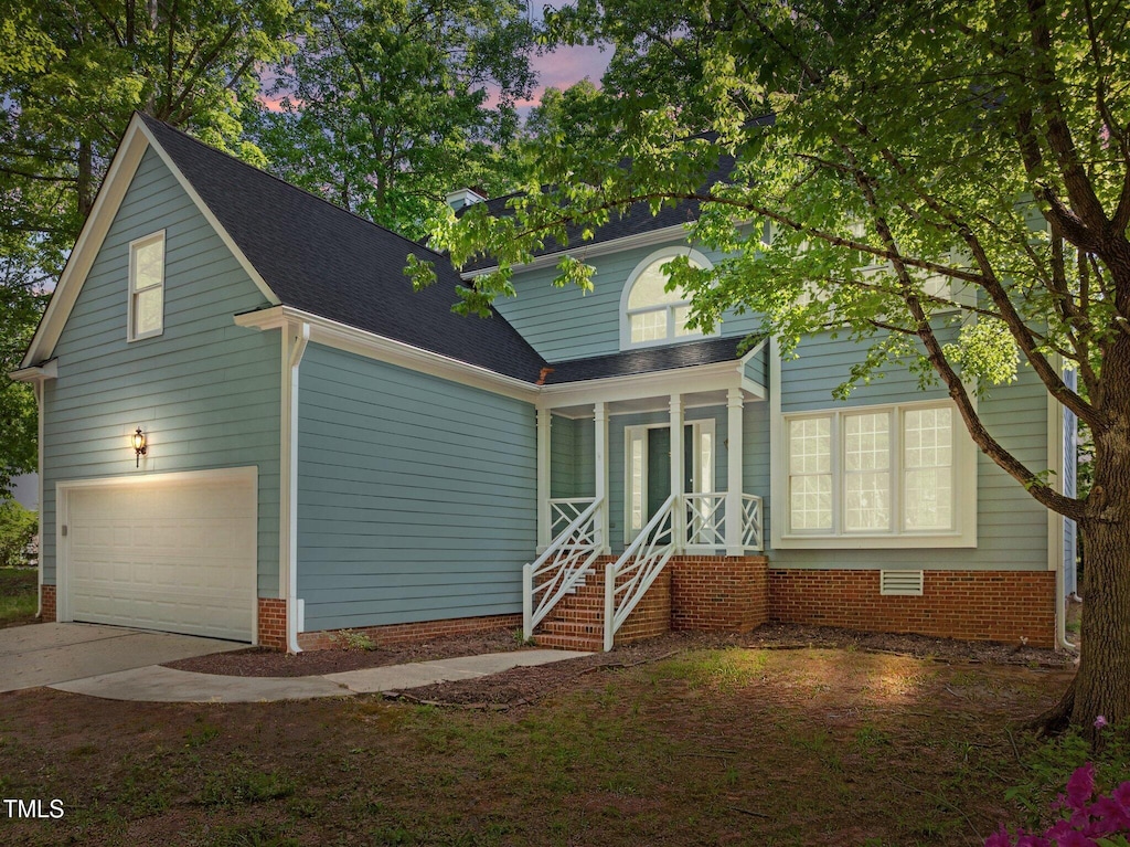 traditional-style house with concrete driveway, a shingled roof, an attached garage, and covered porch