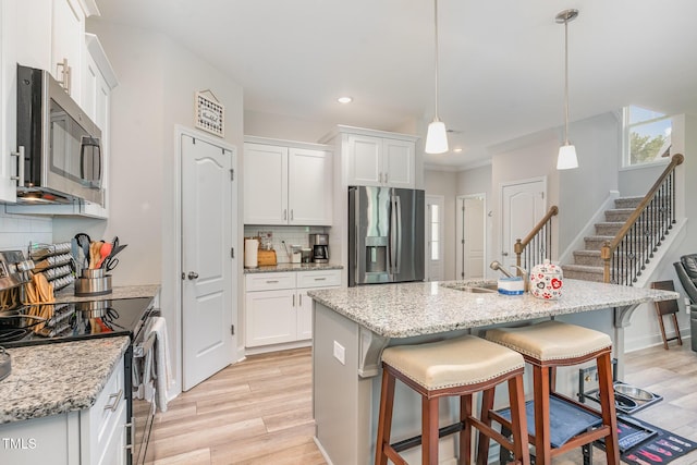 105 Forest Wood Dr, Salemburg, NC 28385 - kitchen with white cabinets, a breakfast bar, light wood-style floors, stainless steel appliances, and backsplash