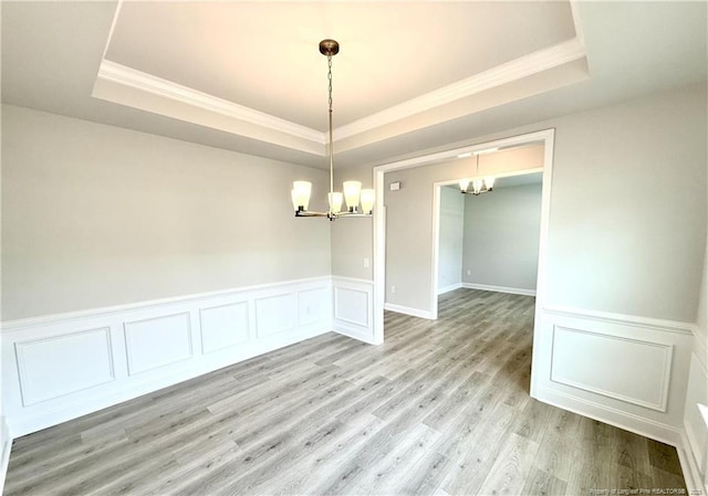 unfurnished dining area with crown molding, a tray ceiling, and a notable chandelier
