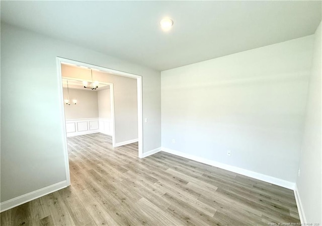 spare room featuring a chandelier, a wainscoted wall, light wood-style flooring, and baseboards
