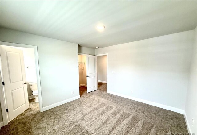 unfurnished bedroom with a walk in closet, a closet, carpet flooring, and baseboards