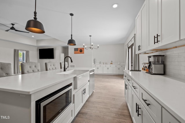kitchen featuring tasteful backsplash, a sink, light countertops, ceiling fan with notable chandelier, and stainless steel appliances