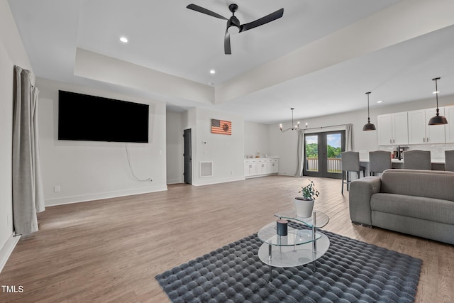 living area featuring baseboards, ceiling fan with notable chandelier, light wood-style flooring, and visible vents