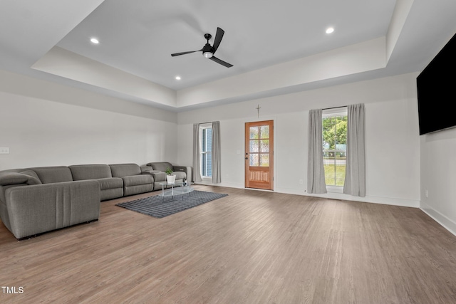 living area with ceiling fan, wood finished floors, baseboards, a tray ceiling, and recessed lighting