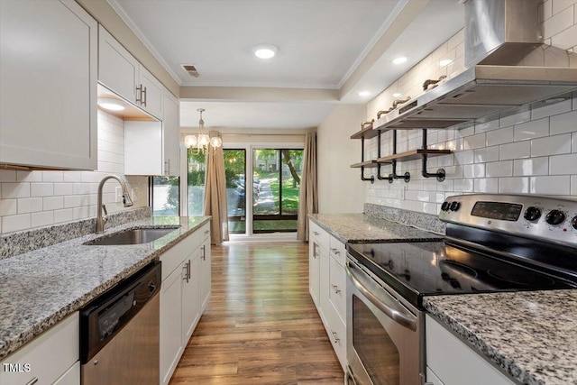 kitchen with wall chimney range hood, white cabinets, a sink, light wood-style flooring, and stainless steel appliances