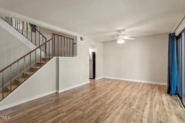 unfurnished living room featuring stairway, baseboards, a ceiling fan, and wood finished floors