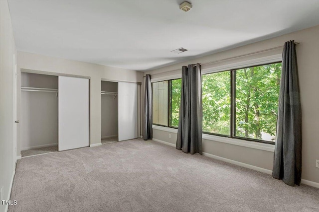 unfurnished bedroom with carpet floors, baseboards, two closets, and visible vents