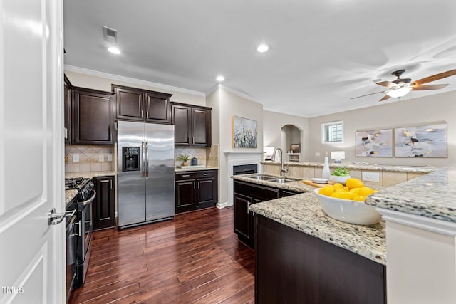 kitchen with stainless steel appliances, a sink, arched walkways, dark wood-type flooring, and dark brown cabinets