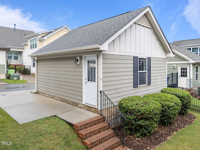 rear view of property featuring board and batten siding, fence, roof with shingles, and a patio area