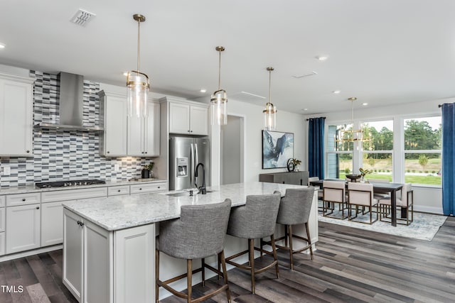 kitchen featuring a kitchen island with sink, decorative backsplash, stainless steel appliances, dark wood-style floors, and wall chimney exhaust hood