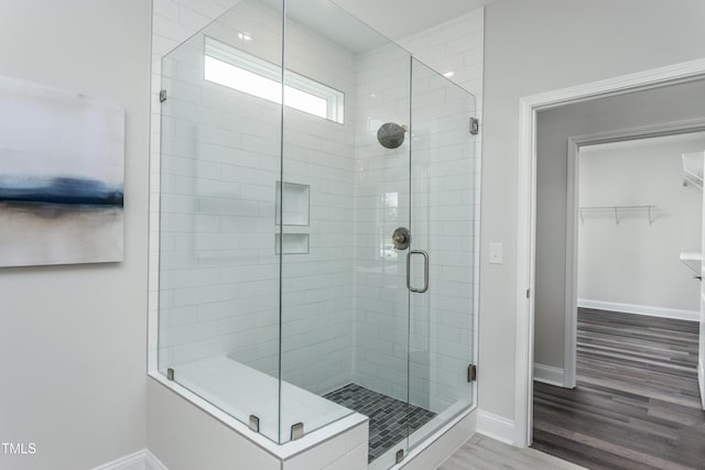 full bathroom featuring a stall shower, a walk in closet, wood finished floors, and baseboards