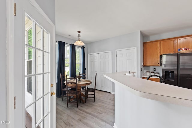 kitchen with stainless steel fridge with ice dispenser, brown cabinetry, light wood finished floors, decorative light fixtures, and light countertops
