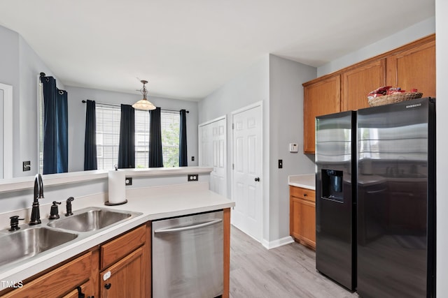 kitchen with refrigerator with ice dispenser, dishwasher, brown cabinetry, a sink, and light wood-style floors