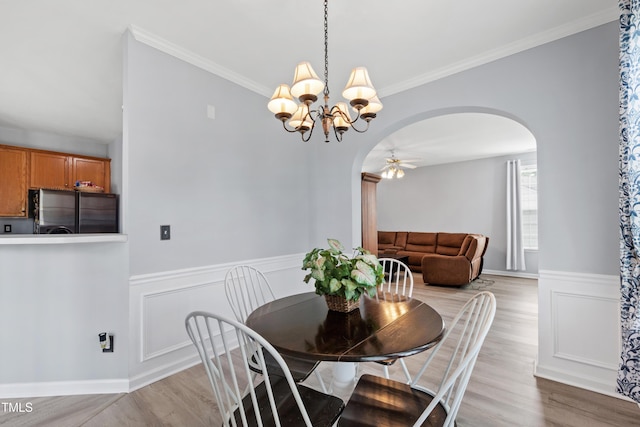 dining area with arched walkways, a chandelier, light wood-style flooring, ceiling fan, and wainscoting