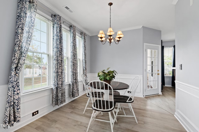 dining area with a chandelier, a wainscoted wall, light wood-type flooring, healthy amount of natural light, and crown molding
