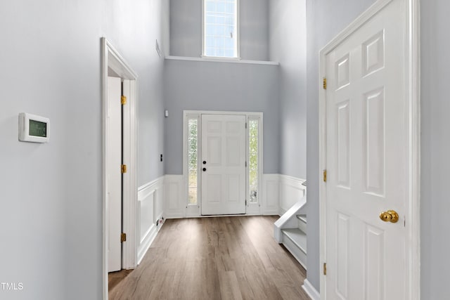 foyer entrance with wainscoting, a high ceiling, wood finished floors, and a decorative wall