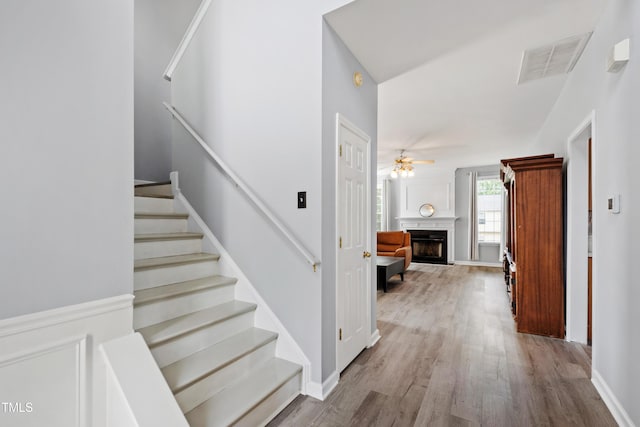 staircase with wood finished floors, ceiling fan, a premium fireplace, and baseboards