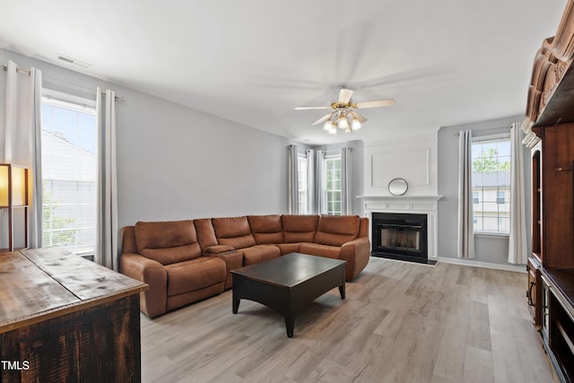living room featuring light wood-type flooring, healthy amount of natural light, ceiling fan, and a fireplace
