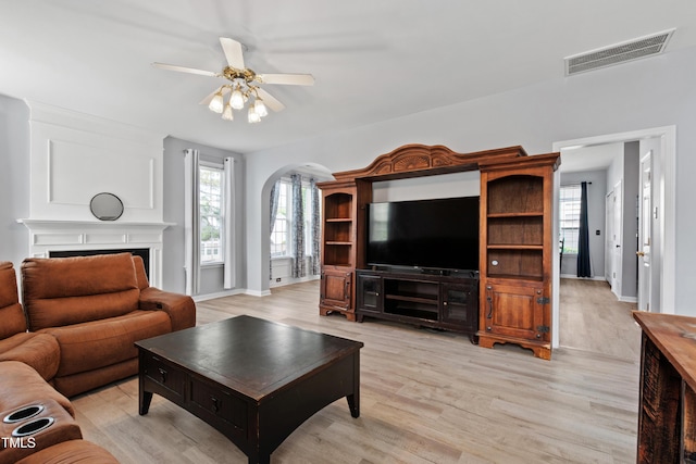 living area with arched walkways, light wood-style floors, and ceiling fan