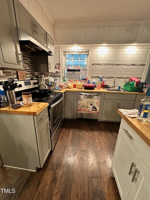 kitchen with brick wall, wooden counters, dark wood-style floors, under cabinet range hood, and stainless steel appliances