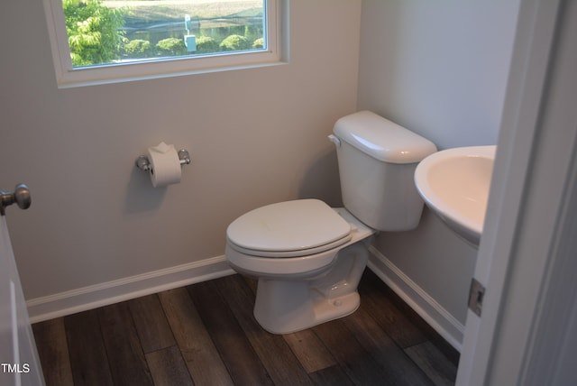half bath with baseboards, toilet, and wood finished floors