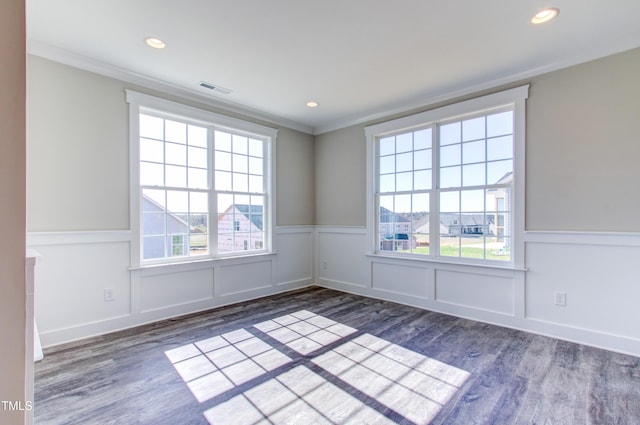 spare room featuring crown molding, a wainscoted wall, visible vents, and wood finished floors