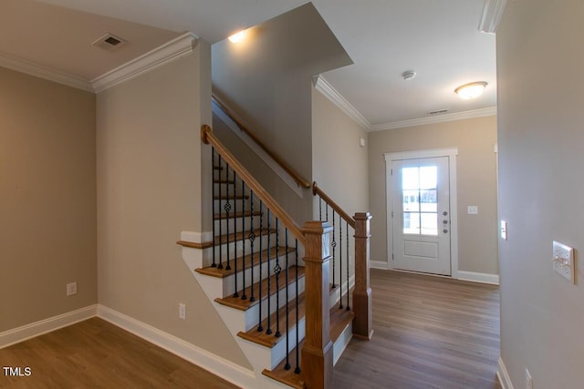 stairway with visible vents, wood finished floors, ornamental molding, and baseboards