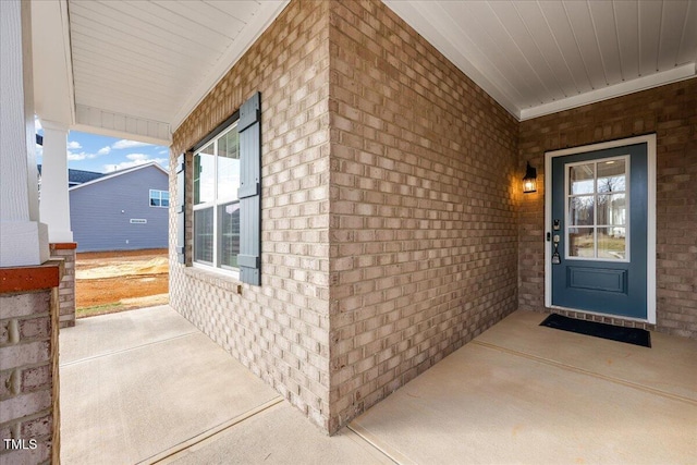 entrance to property featuring a porch and brick siding