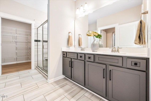 bathroom featuring double vanity, a shower stall, baseboards, and a sink