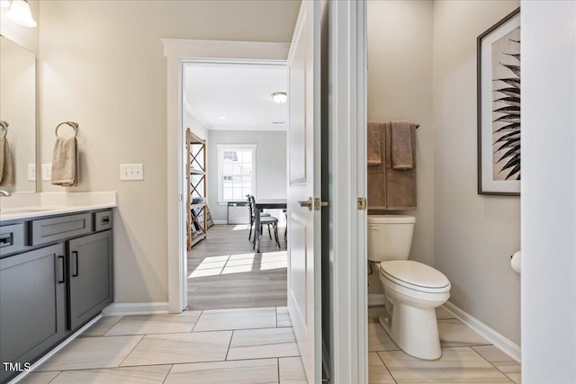 bathroom with vanity, toilet, ornamental molding, and baseboards