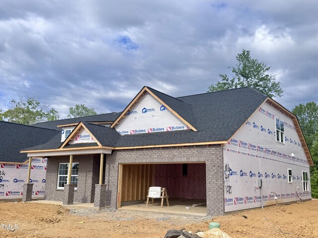 view of front of home with roof with shingles, brick siding, and an attached garage