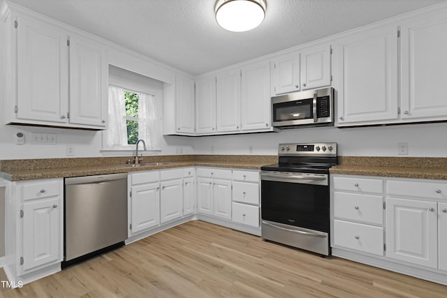 kitchen featuring a textured ceiling, a sink, white cabinets, stainless steel appliances, and light wood-style flooring