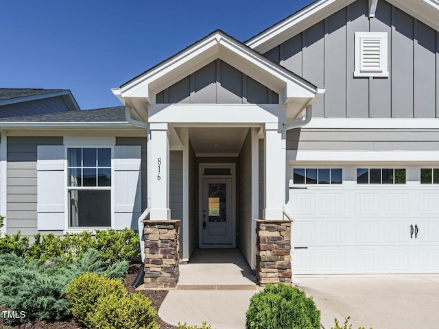 property entrance with board and batten siding, roof with shingles, concrete driveway, and stone siding