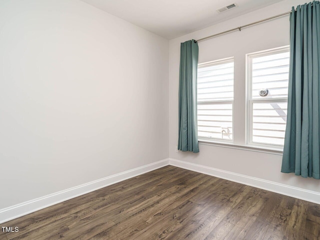 spare room featuring baseboards, dark wood-style floors, and visible vents