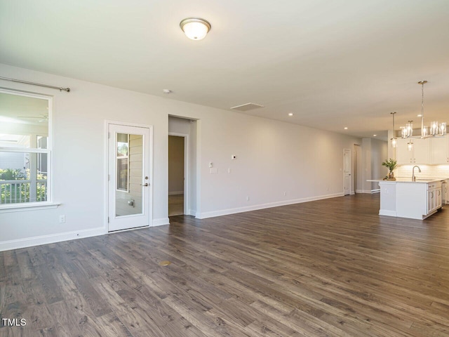 unfurnished living room with a sink, baseboards, and dark wood-type flooring