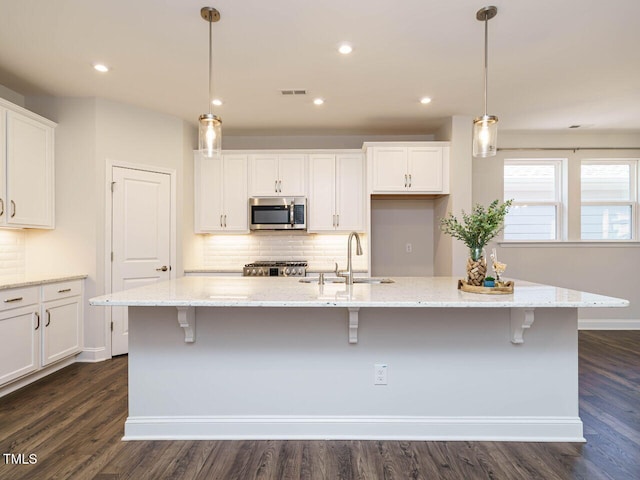 kitchen featuring visible vents, stove, a sink, stainless steel microwave, and white cabinetry