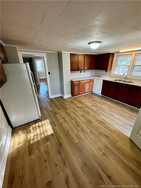 kitchen with freestanding refrigerator, light wood-style floors, light countertops, a sink, and baseboards