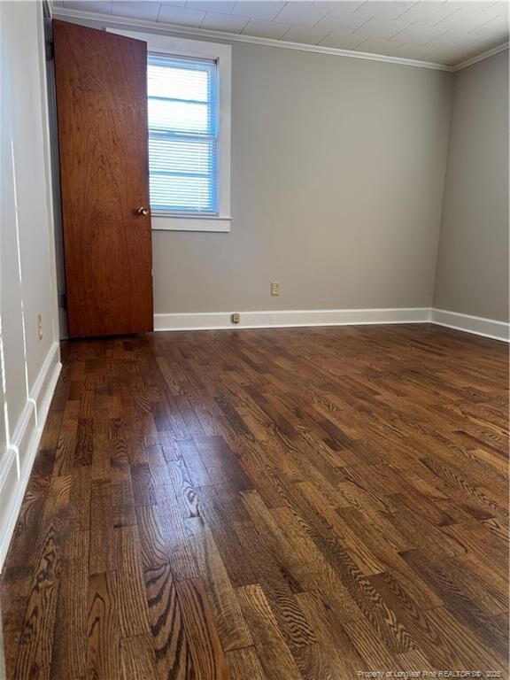 unfurnished room featuring dark wood finished floors, baseboards, and crown molding