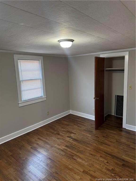 unfurnished bedroom featuring ornamental molding, a closet, and dark wood finished floors