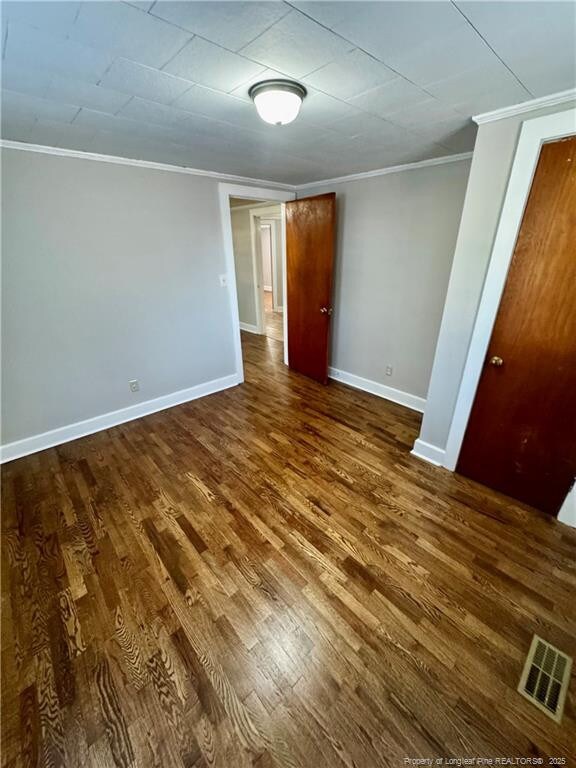 unfurnished bedroom featuring dark wood-type flooring, visible vents, crown molding, and baseboards
