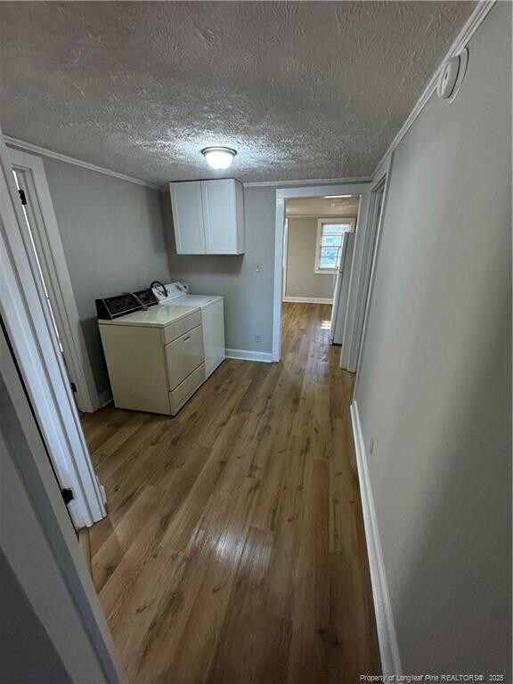 clothes washing area with light wood finished floors, cabinet space, washing machine and dryer, crown molding, and a textured ceiling