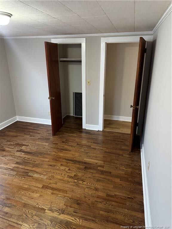 unfurnished bedroom featuring baseboards, ornamental molding, dark wood-style flooring, and a closet