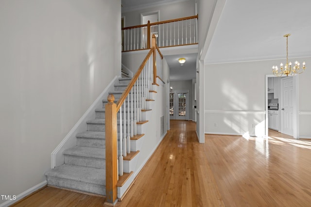 stairs featuring wood-type flooring, baseboards, crown molding, and an inviting chandelier