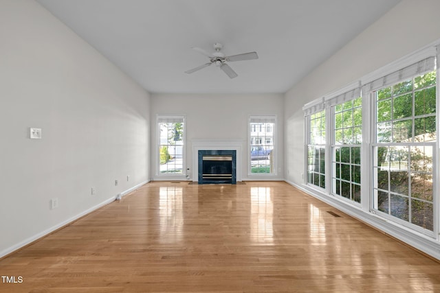 unfurnished living room with visible vents, baseboards, ceiling fan, light wood finished floors, and a premium fireplace