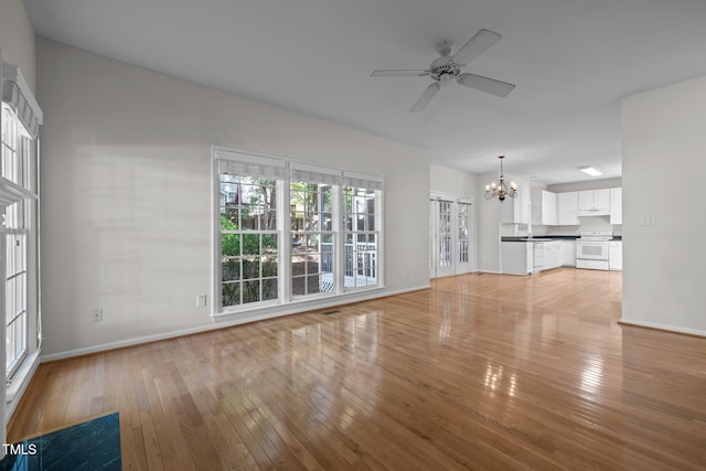 unfurnished living room featuring light wood-style floors, plenty of natural light, ceiling fan with notable chandelier, and baseboards